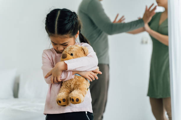 Sad Chinese child holding soft toy with parents having argument in the background
