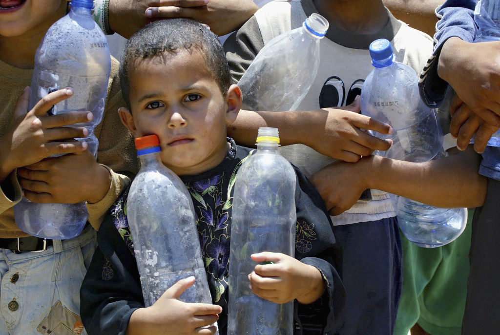 BEIT HANOUN, GAZA STRIP - JULY 06:  Palestinian children carry empty bottles as they look for water on July 6, 2004, in the northern Gaza Strip town of Beit Hanoun. The Israeli army used tanks and to level bushes and trees in the area believed to be a site where Hamas activists launched al-Qassam rocket attacks into Israel. (Photo by Abid Katib/Getty Images)
